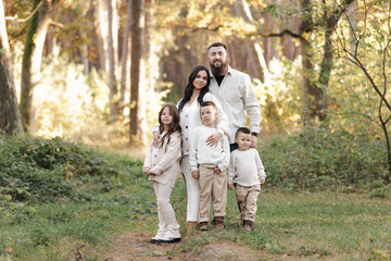 Portrait of big family outdoors. Young Stylish bearded dad with little son on shoulder, beautiful brunette mom, child boy and daughter in autumn park, smiling and looking at camera. Happy family day
