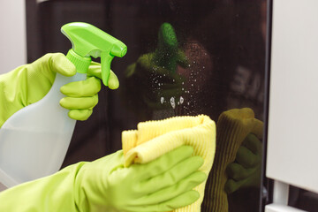 Close up of hands with protective gloves wiping and spraying closed door of oven. House cleaning concept