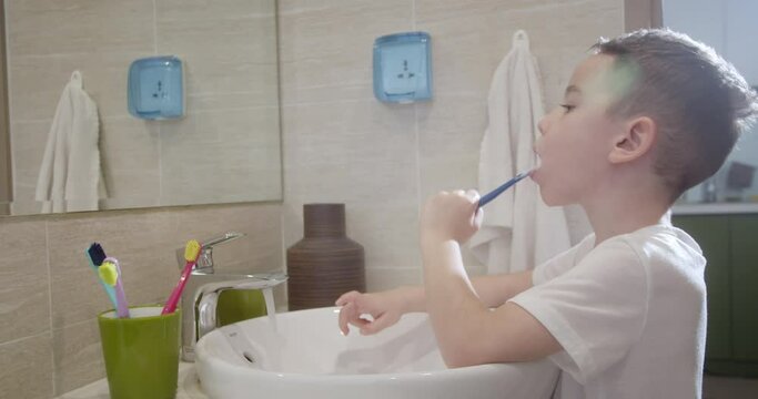 Little boy brushing teeth. Portrait cute child brushing teeth in bathroom and smiling. Happy baby daily healthcare routine. Caucasian kid brushing looking at mirror at home. Lifestyle. 4K