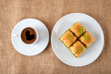 Pistachio baklava on a white plate with Turkish coffee.A plate of traditional baklava on burlap sack