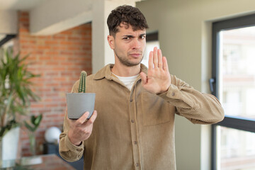 young handsome man looking serious showing open palm making stop gesture. cactus plant concept