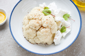 Half of steamed cauliflower head with feta cheese in a white plate, middle close-up, selective focus