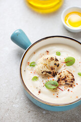 Turquoise serving bowl with cauliflower cream-soup on a beige stone background, vertical shot, middle close-up