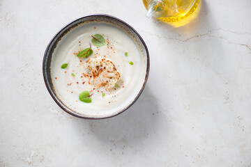 Bowl with cream-soup made of cauliflower cabbage, top view on a light-beige stone background, horizontal shot, copy space