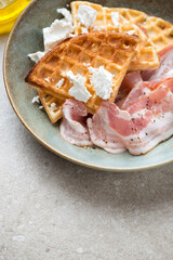 Close-up of belgian waffles with bacon and feta cheese in a plate, vertical shot on a beige stone...