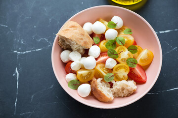 Roseate bowl with mini mozzarella and tomato salad, horizontal shot on a black marble background, elevated view