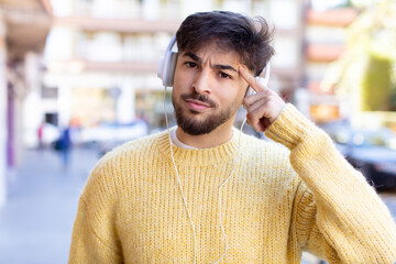 young handsome man looking surprised, realizing a new thought, idea or concept. listening music with headphones