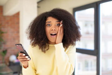 pretty afro black woman feeling extremely shocked and surprised. smartphone concept