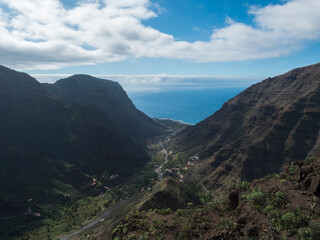 Aerial view from Mirador de Hermigua. Green valley with mountain cliffs, ocean and colorful houses village with terraced fields. La Gomera, Canary island, Spain