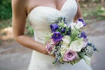 Closeup of a bride holding a bouquet of white, violet and pink roses