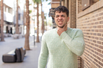 young handsome man feeling ill with a sore throat and flu symptoms, coughing with mouth covered