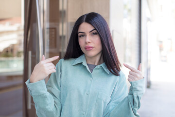 Fototapeta premium young pretty woman with a bad attitude looking proud and aggressive, pointing upwards or making fun sign with hands