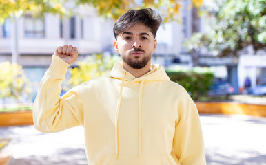 Fototapeta premium young handsome man feeling serious, strong and rebellious, raising fist up, protesting or fighting for revolution