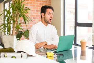 young hispanic man feeling shocked and surprised, looking to copy space on the side with amazed, open-mouthed look. architect concept