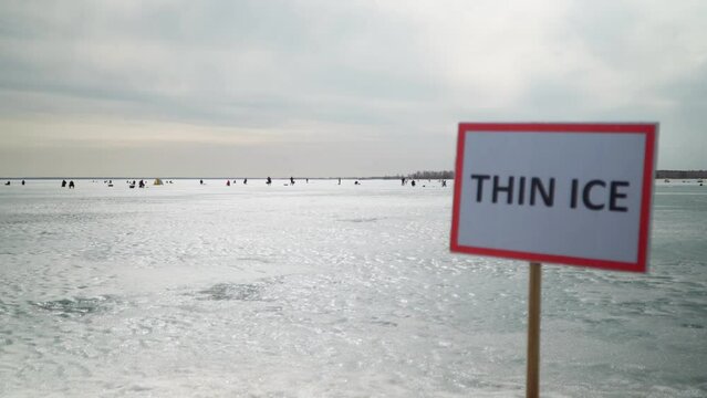 "Thin Ice" sign warning people not to go out on the ice. Sign on the background of fishermen fishing on the ice. Stop, danger, warning.	