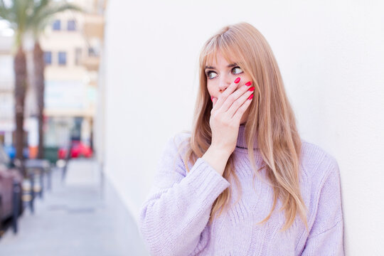 young pretty woman covering mouth with hands with a shocked, surprised expression, keeping a secret or saying oops