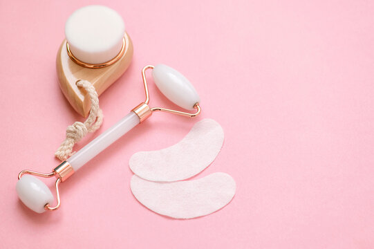 Facial massage set for home spa. Facial roller, massager and patches under the eyes on a pink background. View from above. flat lay