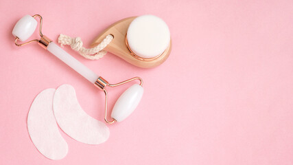 Cosmetics flat lay with copy space.Facial roller, massager and patches under the eyes on a pink background