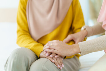 Obraz na płótnie Canvas Asian muslim women encouraging her friend who have a critical problem. Woman touching and holding her friend's hands with empathy.
