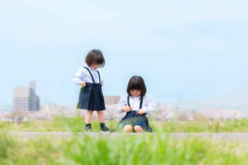 春の河川敷で遊ぶ幼稚園の制服を着た姉妹
