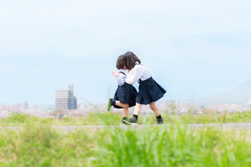 春の河川敷で遊ぶ幼稚園の制服を着た姉妹