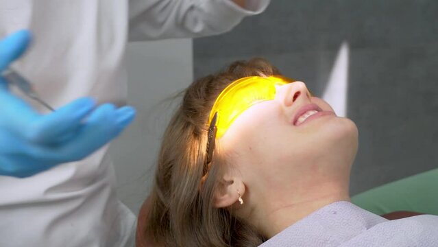 Tooth restoration with filling and polymerization lamp. Young girl during dental filling drying procedure with ultraviolet light curing in dental clinic. Work of doctor and assistant.