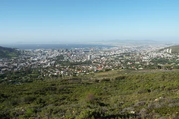 Deurstickers Panoramic view on Cape Town and Atlantic ocean from the foothill of Table Mountain overgrown by green grass and bushes. Townscape is from the base station of cable car which is running on the top. © Lucia