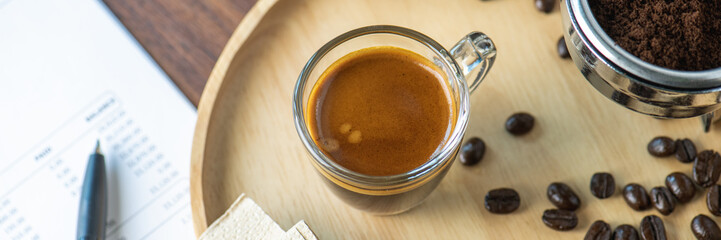 cup of hot Intense coffee dark shot in glass on wooden table with beans with crema. coffee beans and cup full of Intense dark shot coffee in glass cup