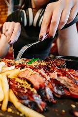 woman hands with fork and knife eating meat ribs in cafe