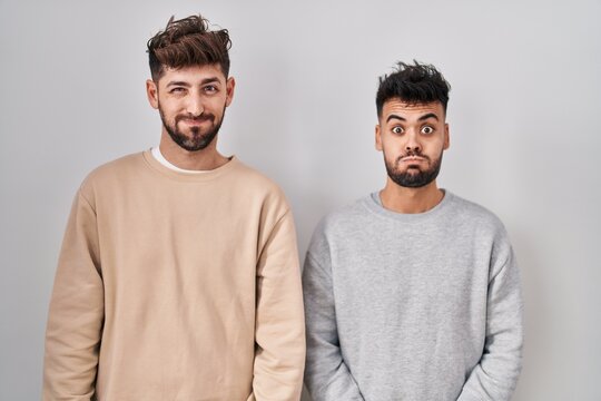 Young homosexual couple standing over white background puffing cheeks with funny face. mouth inflated with air, crazy expression.