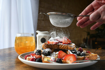 Sprinkling powdered sugar over a plate of French toast topped with berries, breakfast brunch