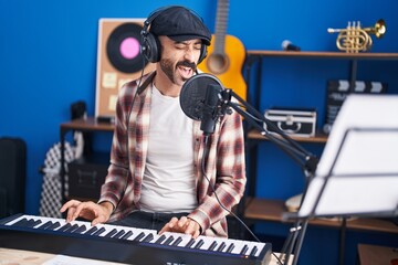 Fototapeta na wymiar Young hispanic man musician playing piano keyboard singing song at music studio