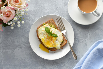 Avocado toast with fried egg over easy & coffee with cream. Breakfast table flat lay, pastel colors