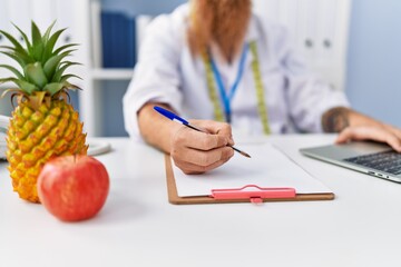 Young redhead man wearing dietician uniform working at clinic