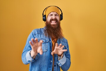 Caucasian man with long beard listening to music using headphones disgusted expression, displeased and fearful doing disgust face because aversion reaction.