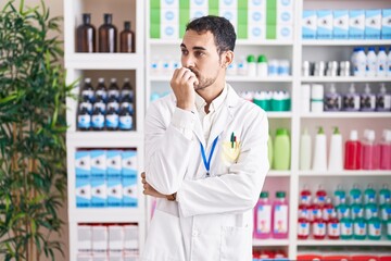 Handsome hispanic man working at pharmacy drugstore looking stressed and nervous with hands on mouth biting nails. anxiety problem.