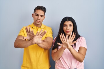 Naklejka premium Young couple standing over isolated background rejection expression crossing arms and palms doing negative sign, angry face