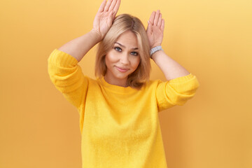 Fototapeta na wymiar Young caucasian woman wearing yellow sweater doing bunny ears gesture with hands palms looking cynical and skeptical. easter rabbit concept.