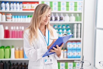 Young blonde woman pharmacist writing on document at pharmacy