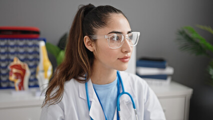 Young beautiful hispanic woman doctor sitting on table looking to the side at clinic