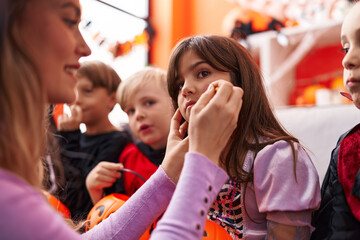 Woman and group of kids wearing costume applying halloween make up at home