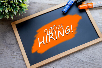 A black chalkboard with the message We are Hiring written on the orange background. Human resource concept