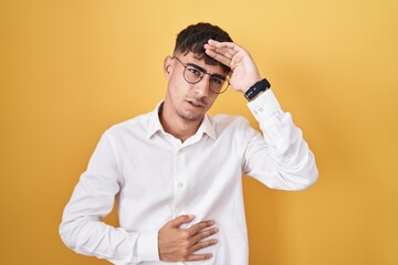 Young hispanic man standing over yellow background touching forehead for illness and fever, flu and cold, virus sick