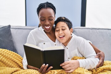Obraz premium African american mother and son reading book sitting on sofa at home