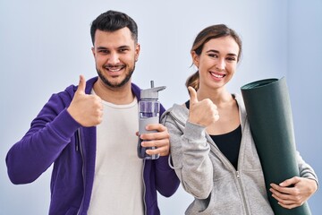 Young hispanic couple wearing sportswear smiling happy and positive, thumb up doing excellent and approval sign