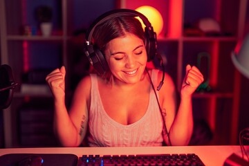 Young blonde woman playing video games wearing headphones very happy and excited doing winner...