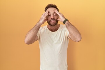 Fototapeta na wymiar Middle age man with beard standing over yellow background trying to open eyes with fingers, sleepy and tired for morning fatigue