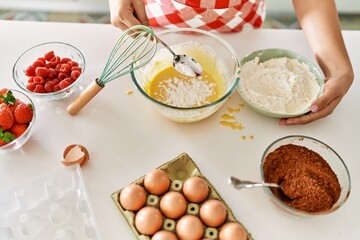 Young beautiful hispanic woman pouring flour on bowl with egg at the kitchen