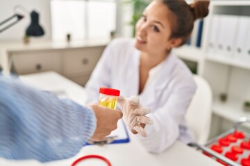 Young beautiful hispanic woman doctor holding urine test tube of patient at clinic