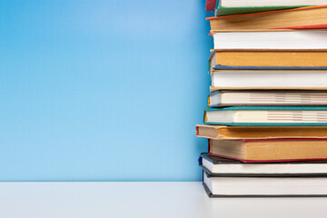 Stack of books in the colored cover lay on the wooden  table and blue backround. Education learning concept